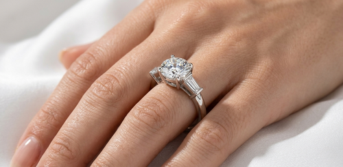 A classic three-stone diamond engagement ring set in white gold displayed elegantly on a model's finger.