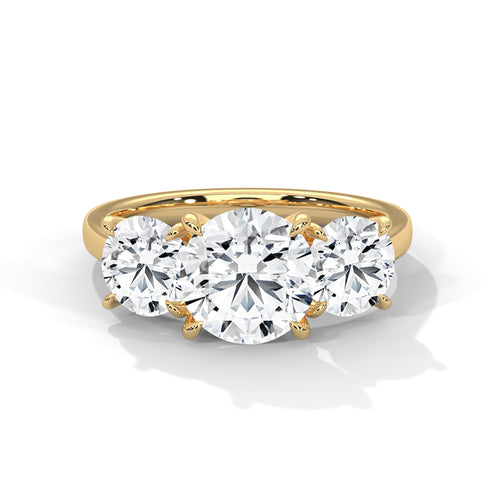 Round brilliant three-stone trilogy engagement ring in yellow gold, close-up view showing pavé band and three-stone setting