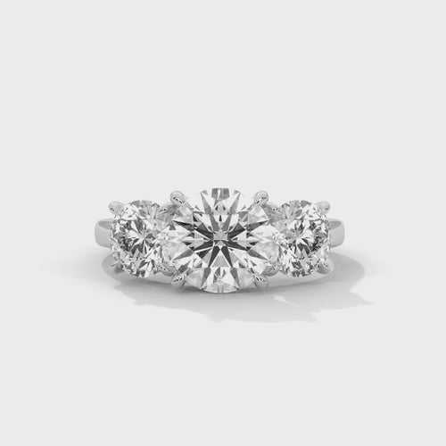 Round brilliant three-stone trilogy engagement ring in white gold, overhead view of three-stone setting and band